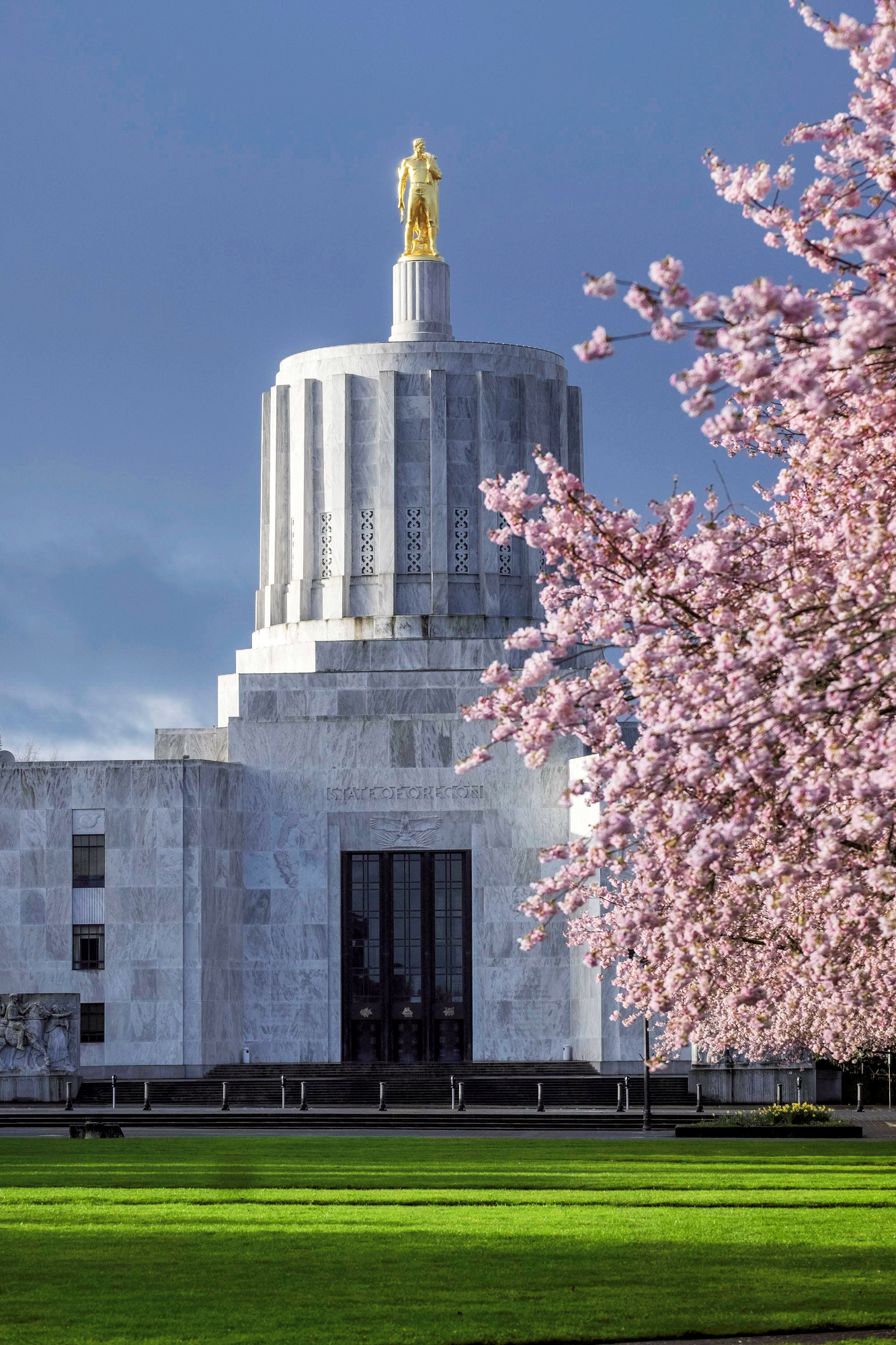 Oregon State Capitol from the Capitol Mall with cherry blossom trees in full bloom.