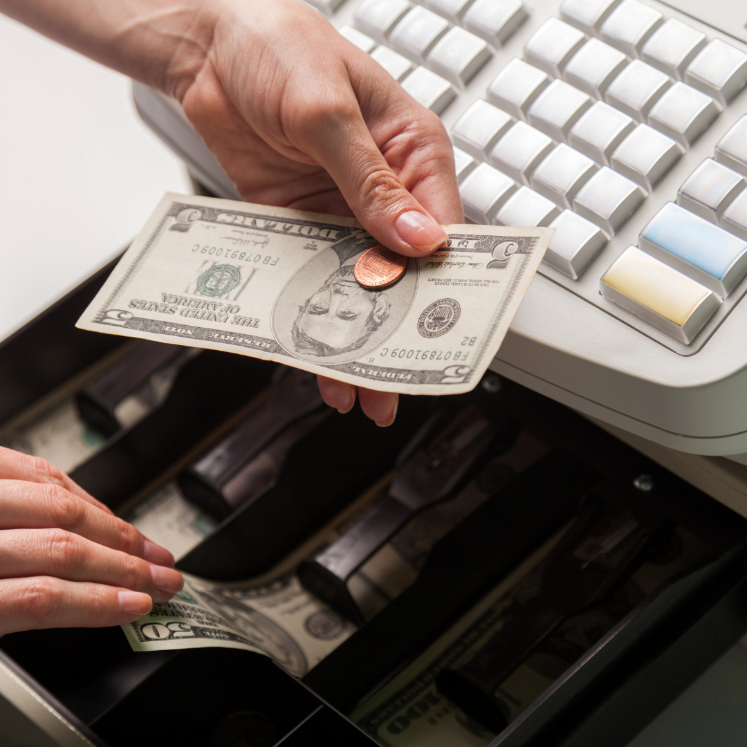 an open cash register drawer showing someone removing a five dollar bill and penny to make change.